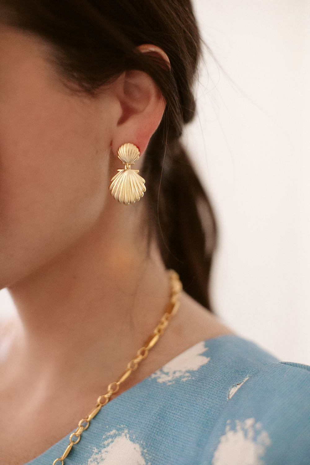 Close-up of model’s left ear wearing Siren’s Song Earrings showcasing linked scalloped shell design plated in 24K gold