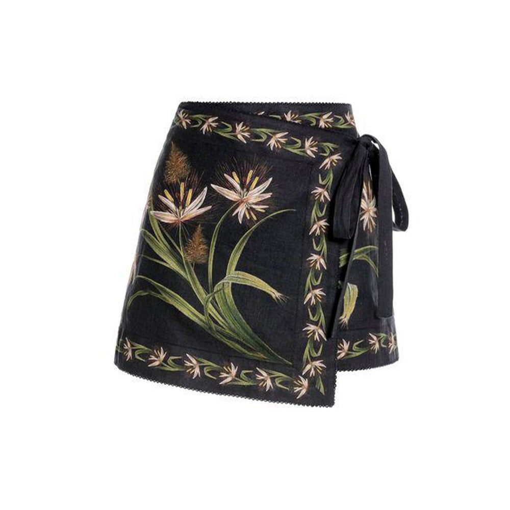 Three quarter view of Luna Azucar Pareo showcasing black mini wrap style with floral placement print and waist tie on white background
