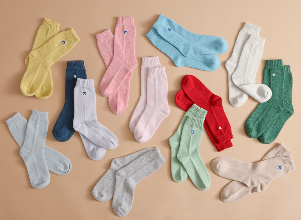 Flat lay of Sleeping Socks showing small embroidered heart and eye motifs in assorted pastel and bold colors on a beige background