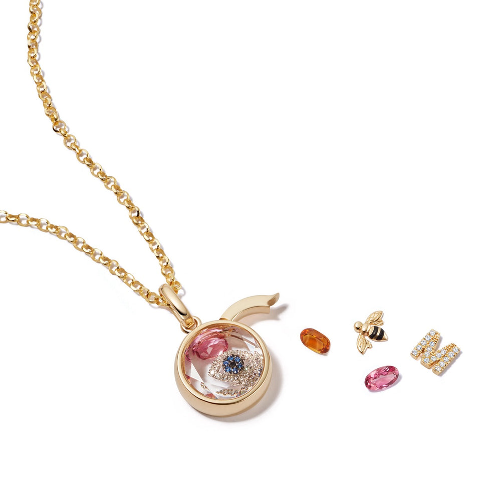 Top-down of small round gold locket showcasing protection evil eye charm and loose gemstone charms