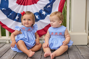 Little English traditional children's clothing.  Flutter sleeve bubble in royal blue mini check fabric and smocking with American flag bunting for baby girls