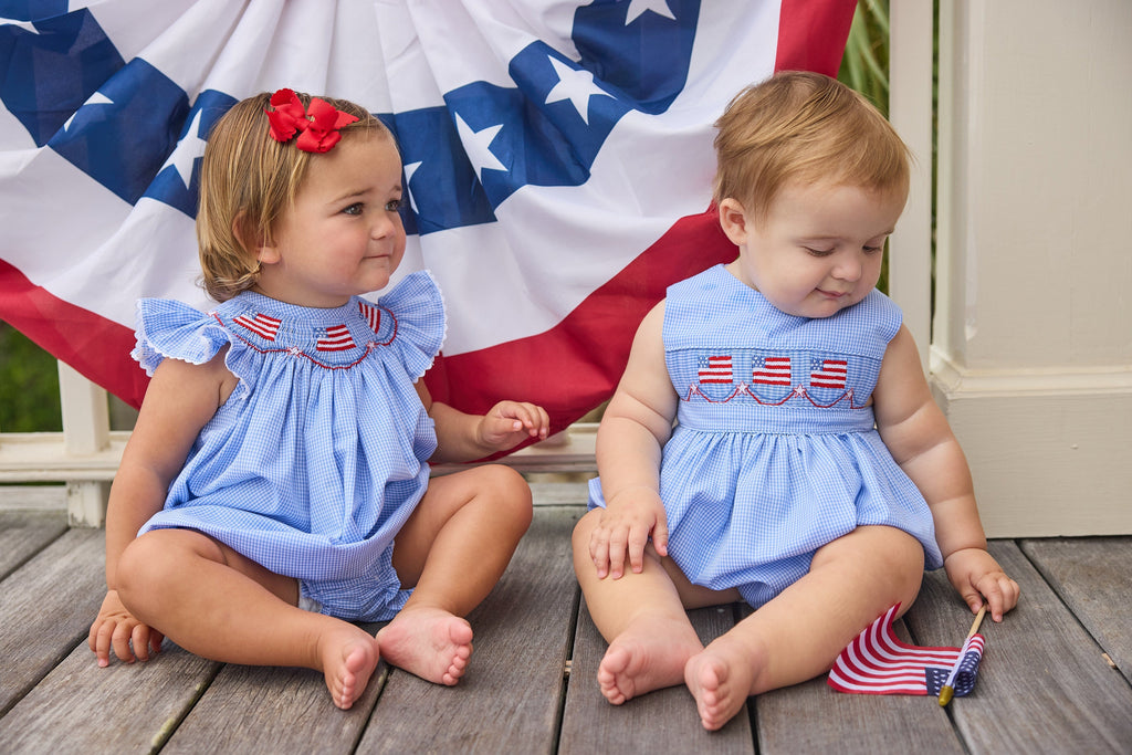 Little English traditional children's clothing.  Sleeveless bubble in royal blue mini check fabric and smocking at the chest with American flag bunting for baby boys