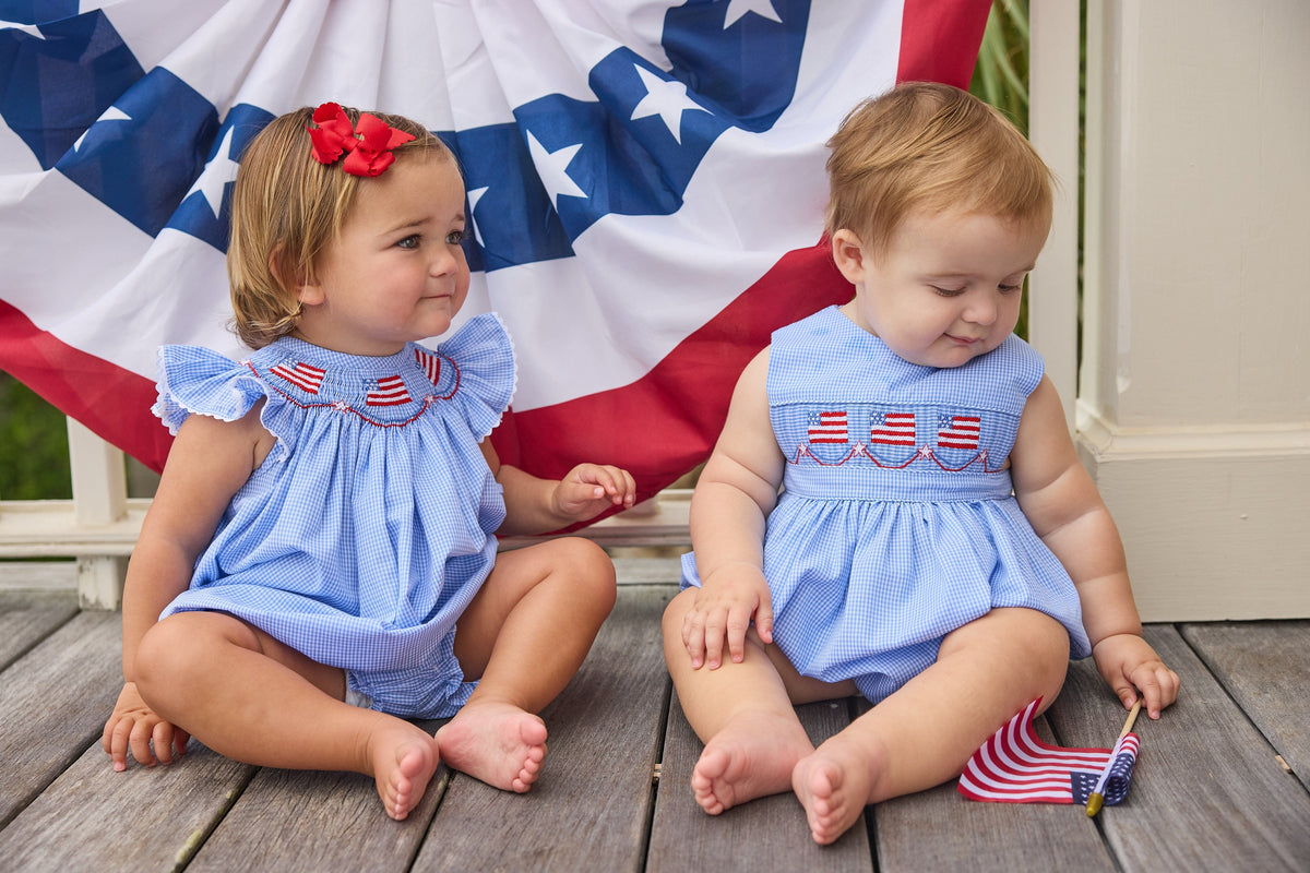 Little English traditional children's clothing.  Sleeveless bubble in royal blue mini check fabric and smocking at the chest with American flag bunting for baby boys