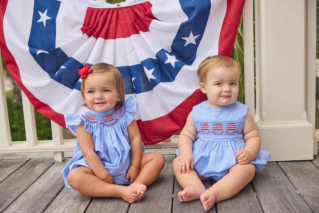 Little English traditional children's clothing.  Sleeveless bubble in royal blue mini check fabric and smocking at the chest with American flag bunting for baby boys