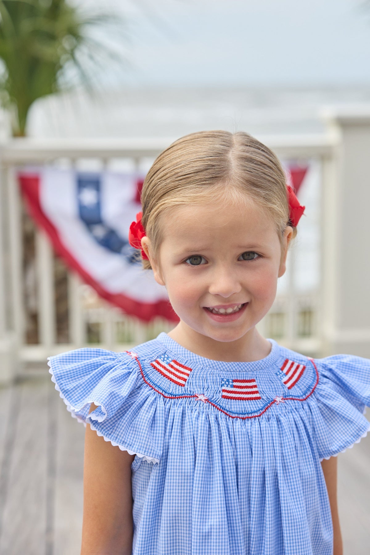 Little English traditional children's clothing. Flutter sleeve dress for toddler girls in royal blue mini gingham with smocking at the collar and American flag bunting