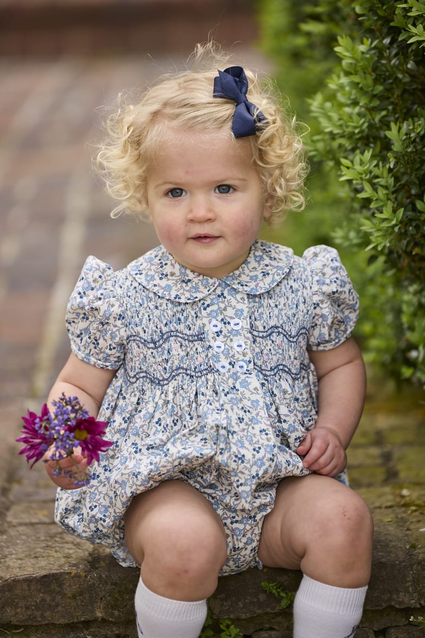 Little English classic children's clothing.  Dressy peter pan bubble for baby girls in blue Wisteria Floral with puff sleeves, ruffle details, and smocking at chest.