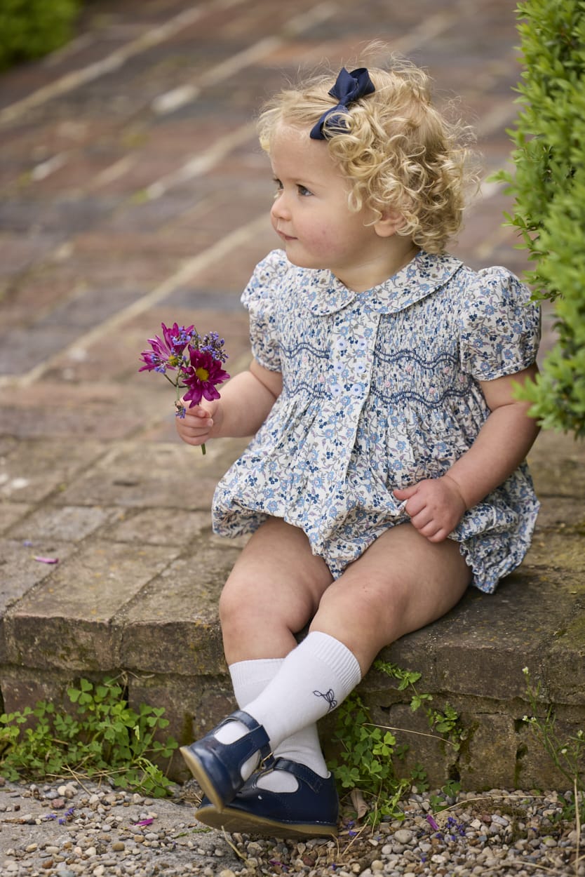 Little English classic children's clothing.  Dressy peter pan bubble for baby girls in blue Wisteria Floral with puff sleeves, ruffle details, and smocking at chest.