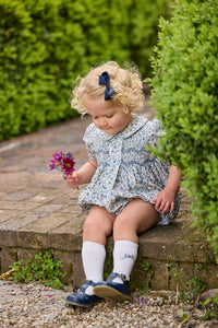 Little English classic children's clothing.  Dressy peter pan bubble for baby girls in blue Wisteria Floral with puff sleeves, ruffle details, and smocking at chest. Paired with white cotton knee high socks with navy bow embroidery