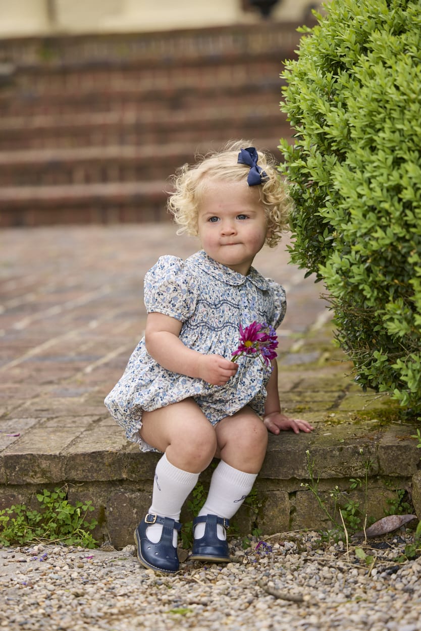 Little English classic children's clothing.  Dressy peter pan bubble for baby girls in blue Wisteria Floral with puff sleeves, ruffle details, and smocking at chest.