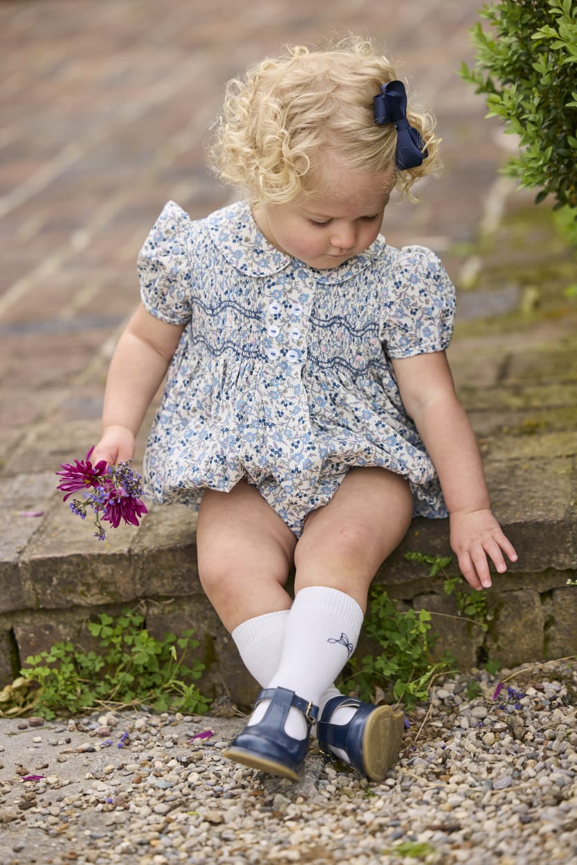 Little English classic children's clothing.  Dressy peter pan bubble for baby girls in blue Wisteria Floral with puff sleeves, ruffle details, and smocking at chest.