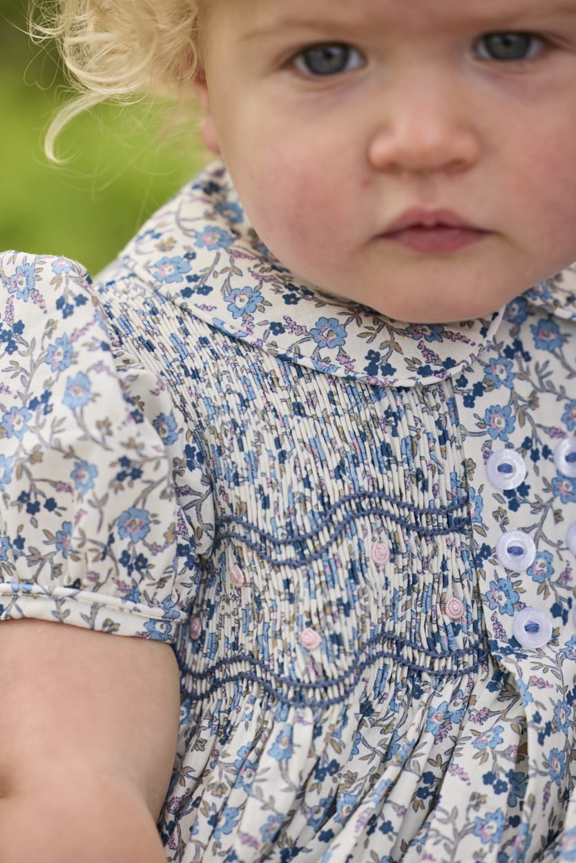 Little English classic children's clothing.  Dressy peter pan bubble for baby girls in blue Wisteria Floral with puff sleeves, ruffle details, and smocking at chest.