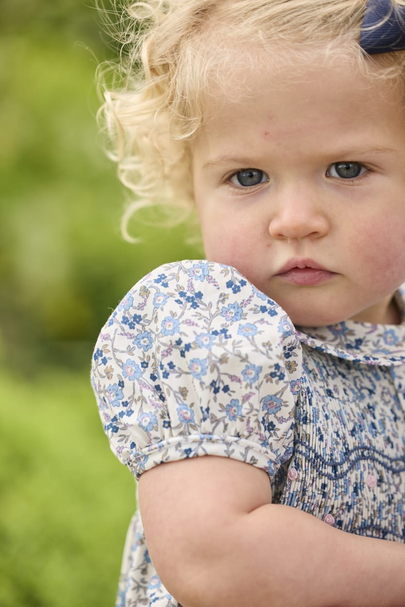 Little English classic children's clothing.  Dressy peter pan bubble for baby girls in blue Wisteria Floral with puff sleeves, ruffle details, and smocking at chest.