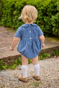 Little English classic children's clothing.  Baby boys stormy blue corduroy peter pan bubble with button tabs and flying mallard smocking across the chest. White knee high socks with mallard embroidery.