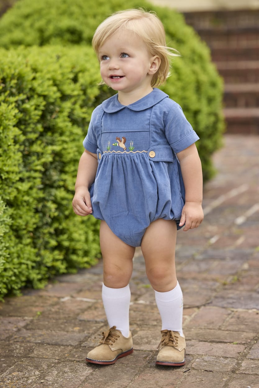 Little English classic children's clothing.  Baby boys stormy blue corduroy peter pan bubble with button tabs and flying mallard smocking across the chest.