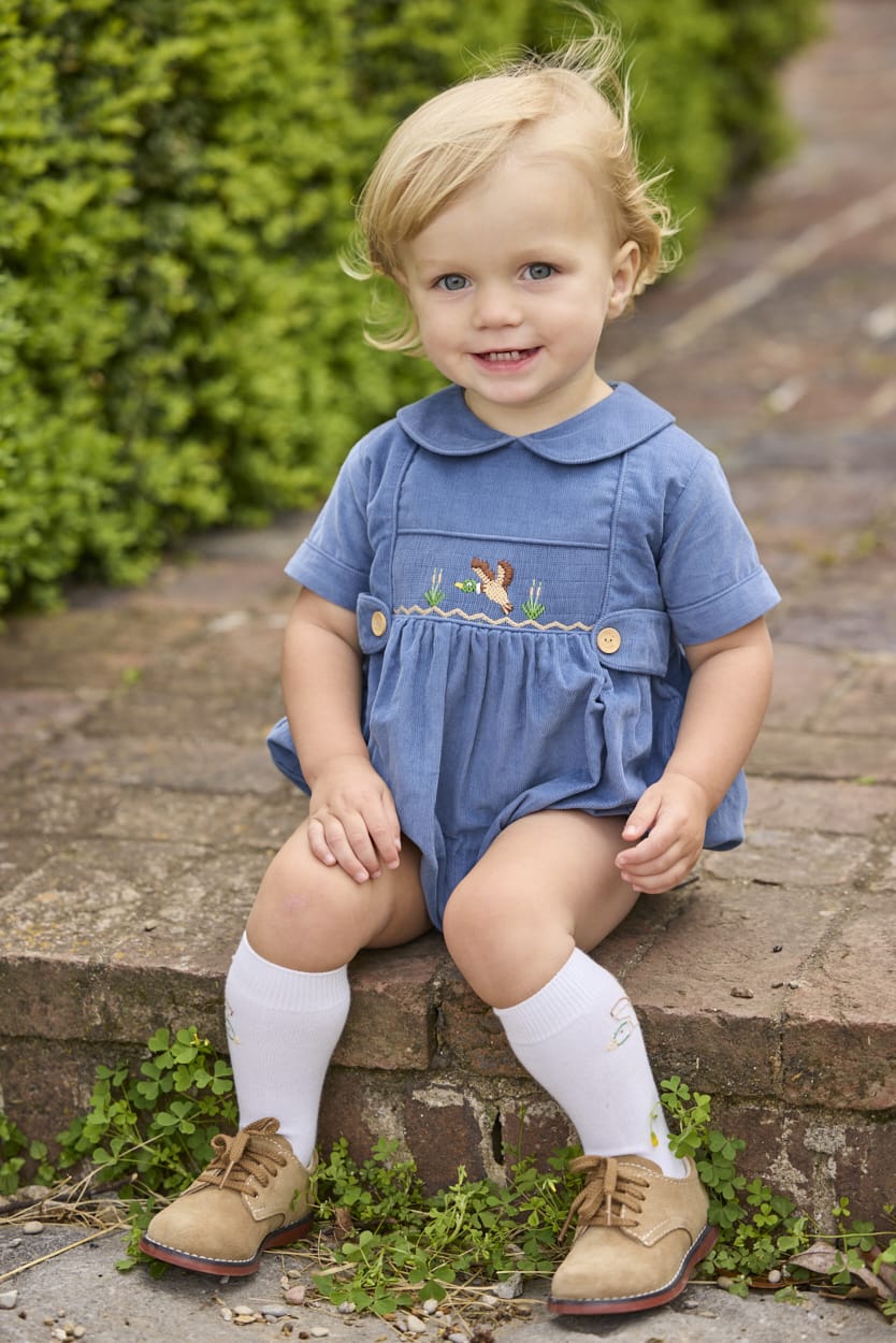 Little English classic children's clothing.  Baby boys stormy blue corduroy peter pan bubble with button tabs and flying mallard smocking across the chest.