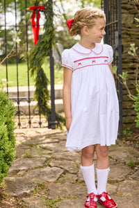 Little English traditional children's clothing.  Puff sleeve white peter pan dress with scalloped collar, red trim, and bow smocking across the chest.  Dressy outfit for little girls for the holiday