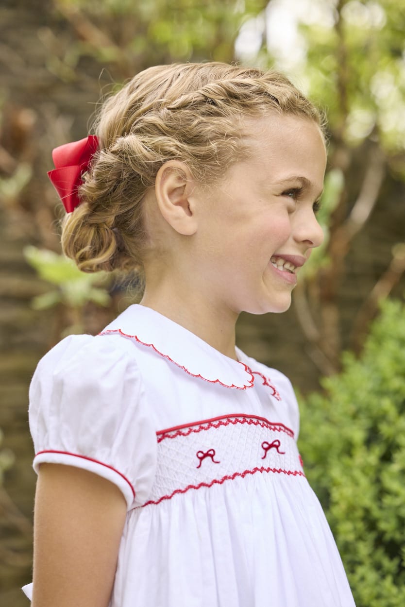 Little English traditional children's clothing.  Puff sleeve white peter pan dress with scalloped collar, red trim, and bow smocking across the chest.  Dressy outfit for little girls for the holiday