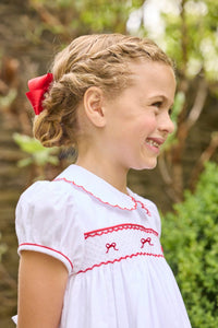 Little English traditional children's clothing.  Puff sleeve white peter pan dress with scalloped collar, red trim, and bow smocking across the chest.  Dressy outfit for little girls for the holiday