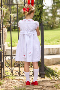 Little English traditional children's clothing.  Puff sleeve white peter pan dress with scalloped collar, red trim, and bow smocking across the chest.  Dressy outfit for little girls for the holiday