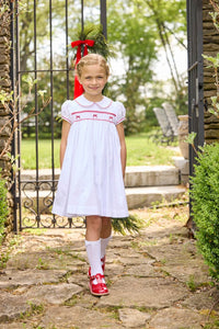 Little English traditional children's clothing.  Puff sleeve white peter pan dress with scalloped collar, red trim, and bow smocking across the chest.  Dressy outfit for little girls for the holiday