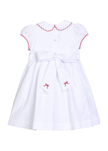 Little English traditional children's clothing.  Puff sleeve white peter pan dress with scalloped collar, red trim, and bow smocking across the chest.  Dressy outfit for little girls for the holiday