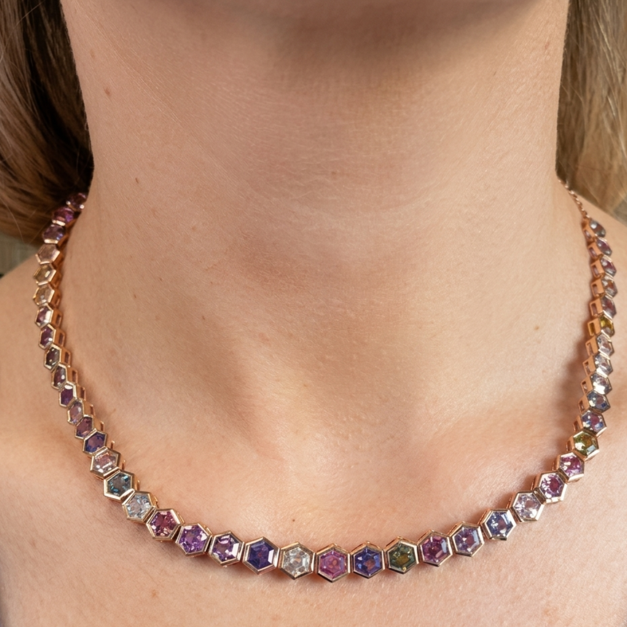 A close-up of a neck adorned with the Spectrum Collar Necklace in Rose Gold, featuring bezel-set multicolor hexagonal sapphires arranged symmetrically for a vibrant, elegant look.