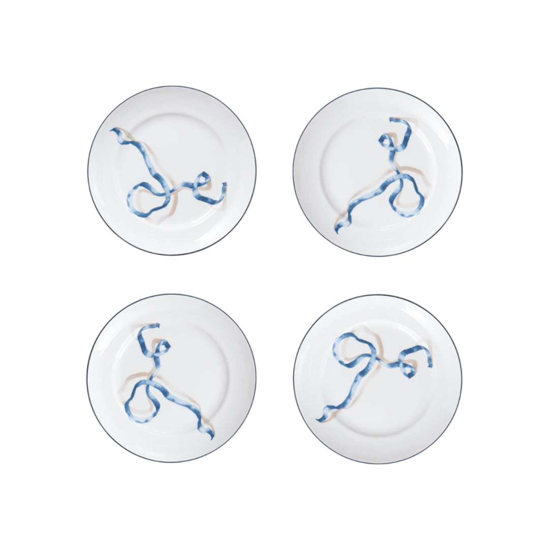 Set of Four Ribbon Desset Plates in Blue. WeÕre willing to bet your favorite foodie has never seen dinner plates quite like these. Designed by artist and designer Adam Charlap Hyman for SprezzÕs holiday collection, these plates feature a 3D-like ribbon design inspired by 17th- and 18th-century paintings. These fun plates are available in two sizes and three colors.