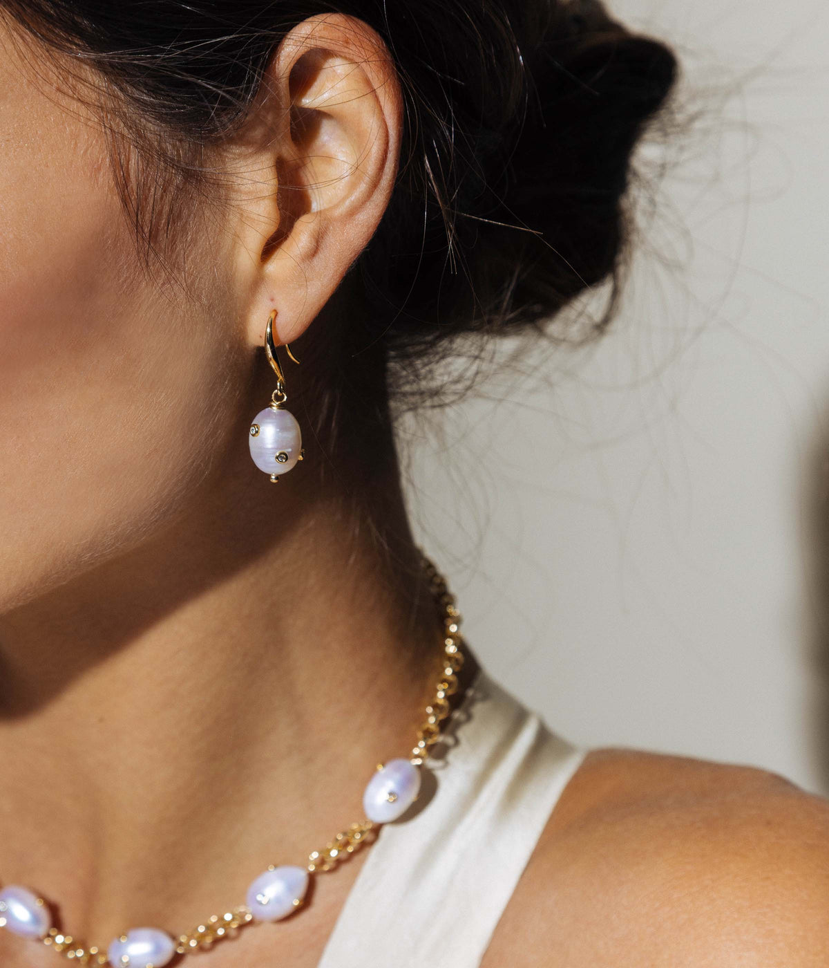 Side view of Geneva Pearl Drop Earrings showcasing a baroque pearl and crystal details on a model