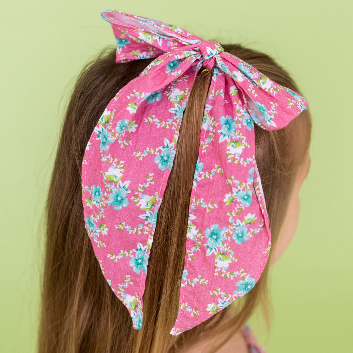 Rear view of Isla Bow showcasing pink floral fabric and long tied tails on a child’s hair against a pale green background