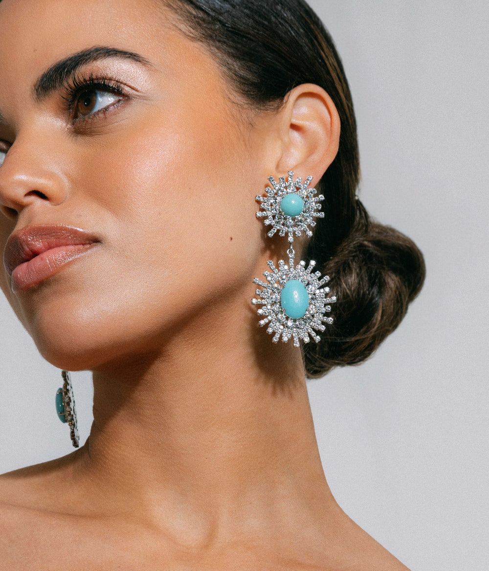 Close-up of Stevie Statement Earrings showing turquoise cabochons in silver-tone sunburst setting on light gray background