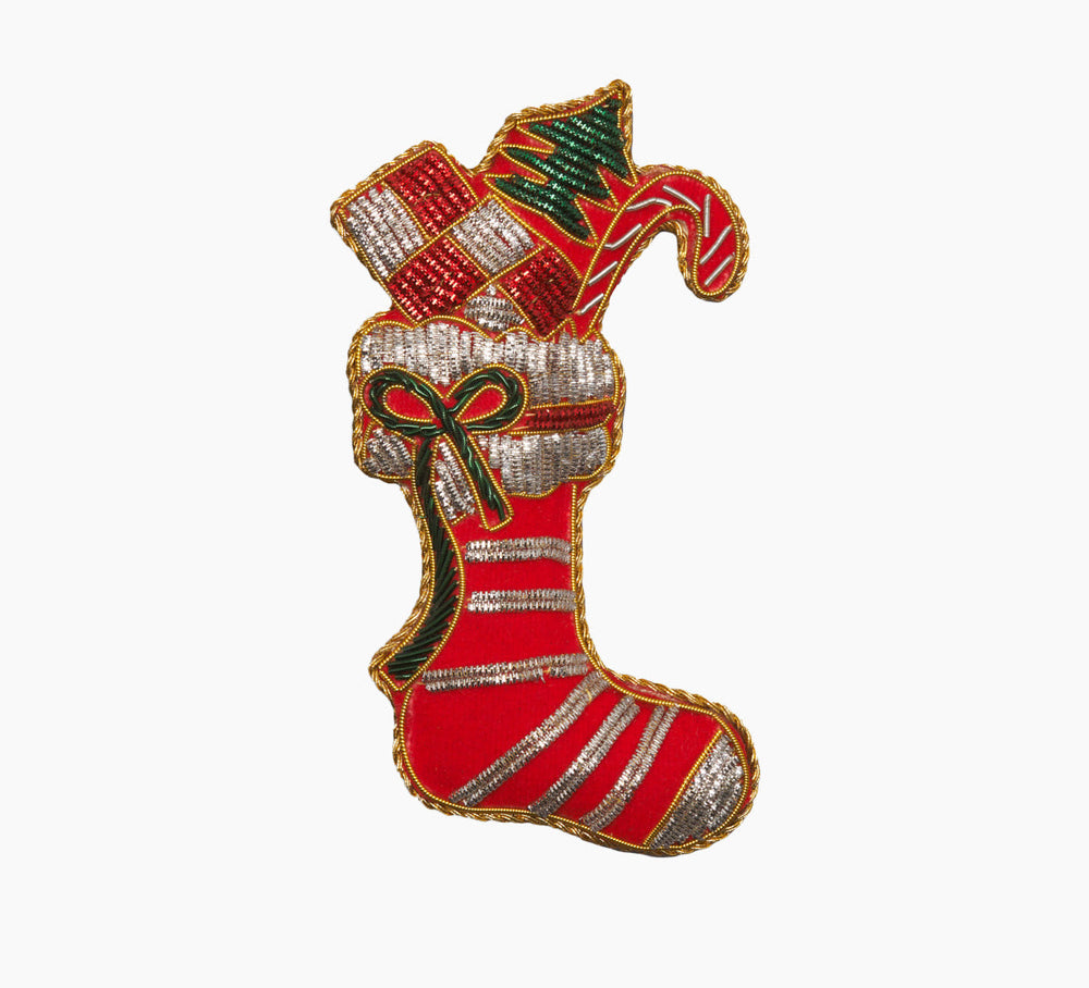 Front view of red velveteen stocking ornament with gold and silver metallic embroidery, hand-stitched beads, green ribbon bow, and candy-cane and gift shapes on white background