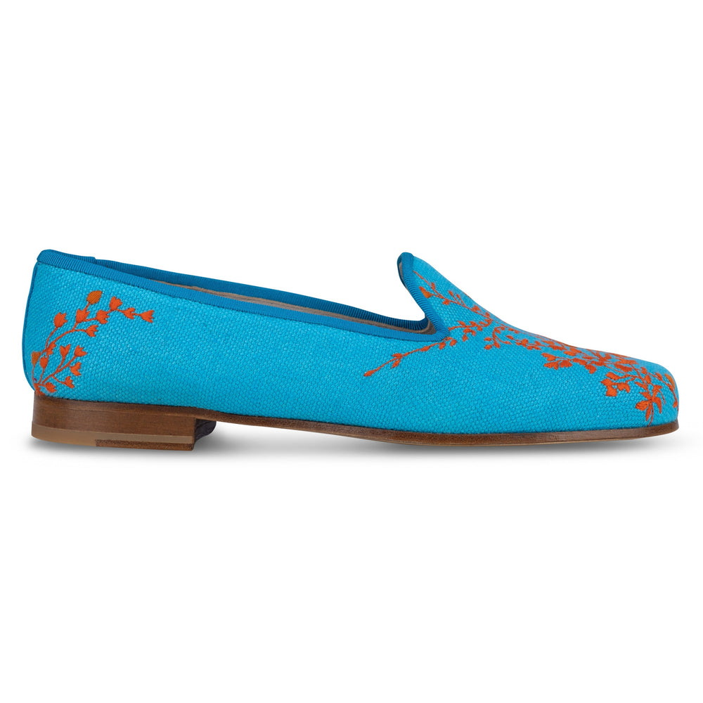 Side view of Fleurs turquoise linen slipper showcasing orange floral embroidery and low stacked wooden heel on white background