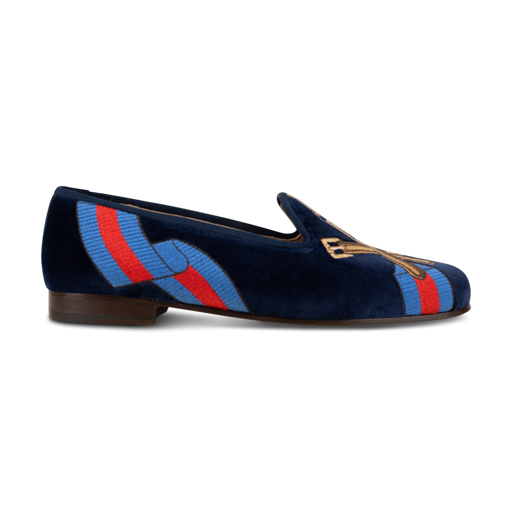 Side view of the Paddock Naval Slipper showcasing navy velvet, striped racing silk embroidery, and leather sole with a white background