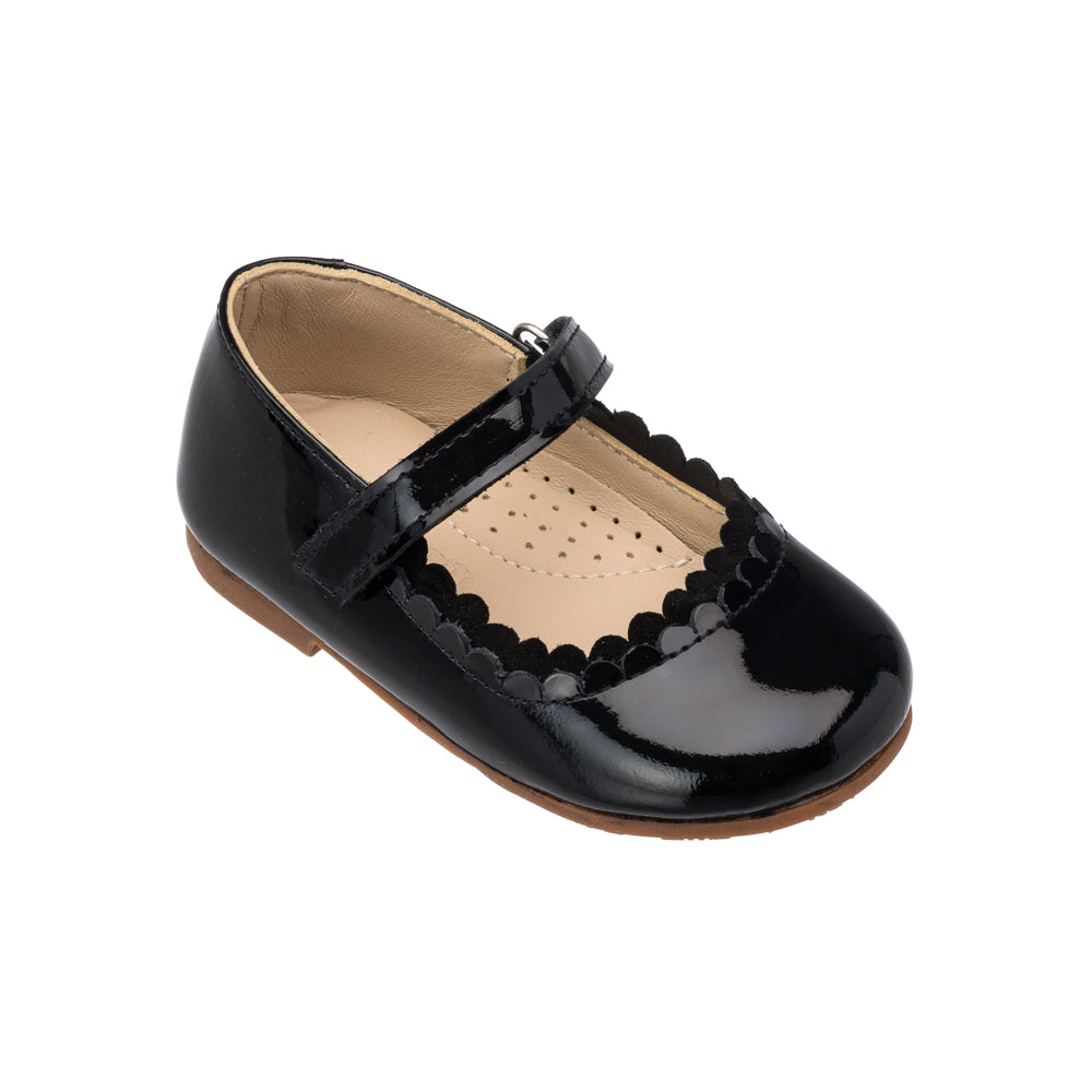 Three quarter view of Toddler Aria flat showcasing black patent leather, scalloped edge and hook and loop strap on white background