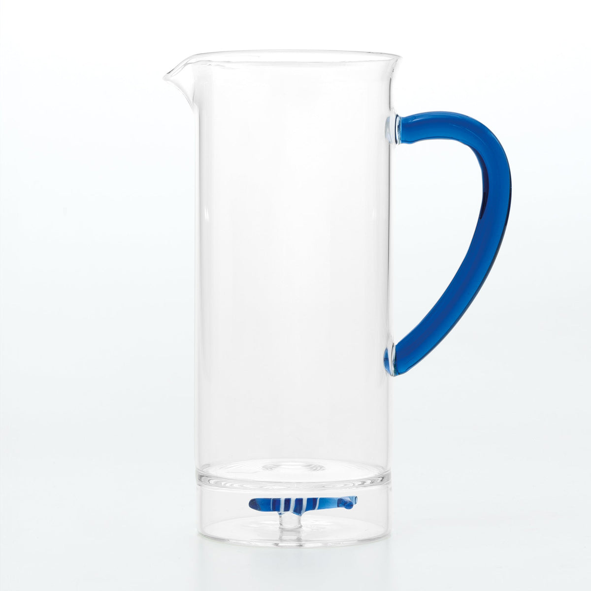 Side view of Teca Mare Carafe with clear cylindrical glass, blue curved handle, spout, and small blue base accent on white