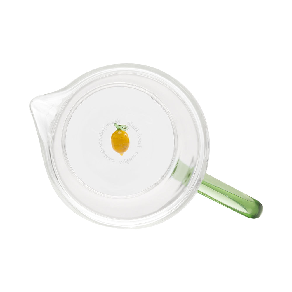 Top view of Teca Frutta glass carafe showing clear body, green handle, and small lemon decoration on white background