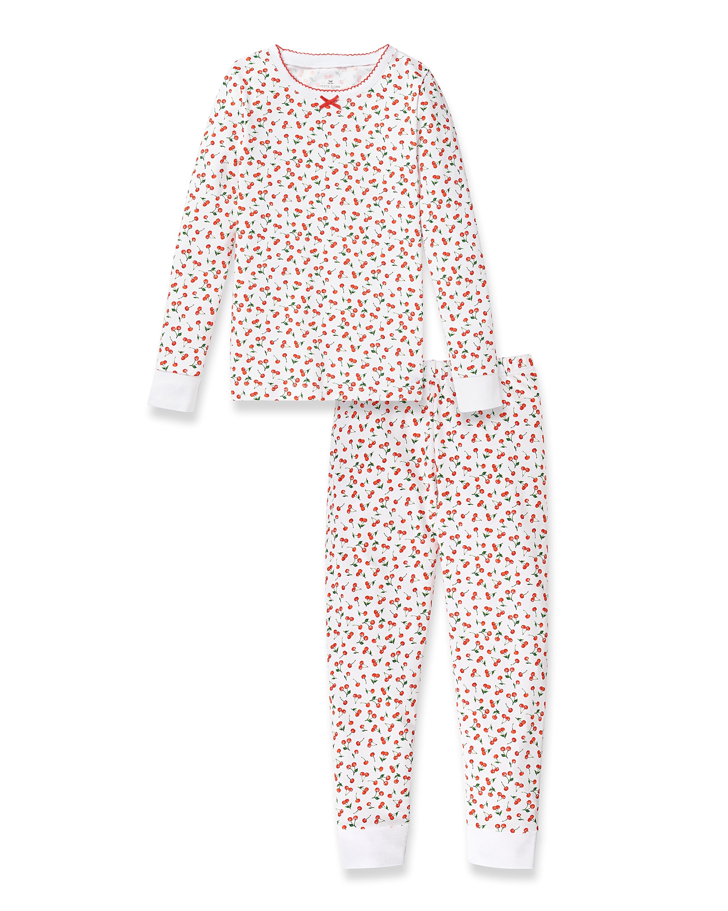 The Petite Plume Kids Pima Snug Fit Pajama Set in Cherry Orchard features a soft white Pima cotton long-sleeve top and bottoms, adorned with red cherry and green leaf print, a charming red bow at the neckline, and finished with red trim.