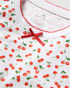 The Kids Pima Snug Fit Pajama Set in Cherry Orchard by Petite Plume features a close-up of the white shirt in luxurious Pima Cotton, adorned with small red cherries and green stems. A tiny red bow decorates the neckline, and decorative red stitching lines the collar edge.