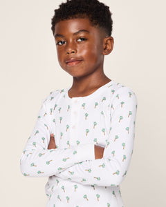 A young boy with short curly hair stands confidently with arms crossed, wearing the Kids Pima Snug Fit Pajama Set in Palmier by Petite Plume.