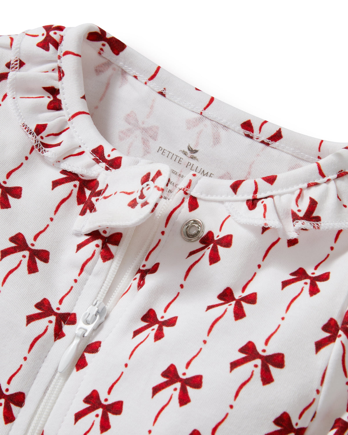Close-up of Baby’s Pima romper neckline showing front zipper and snap, ruffle collar, and red bow print on white