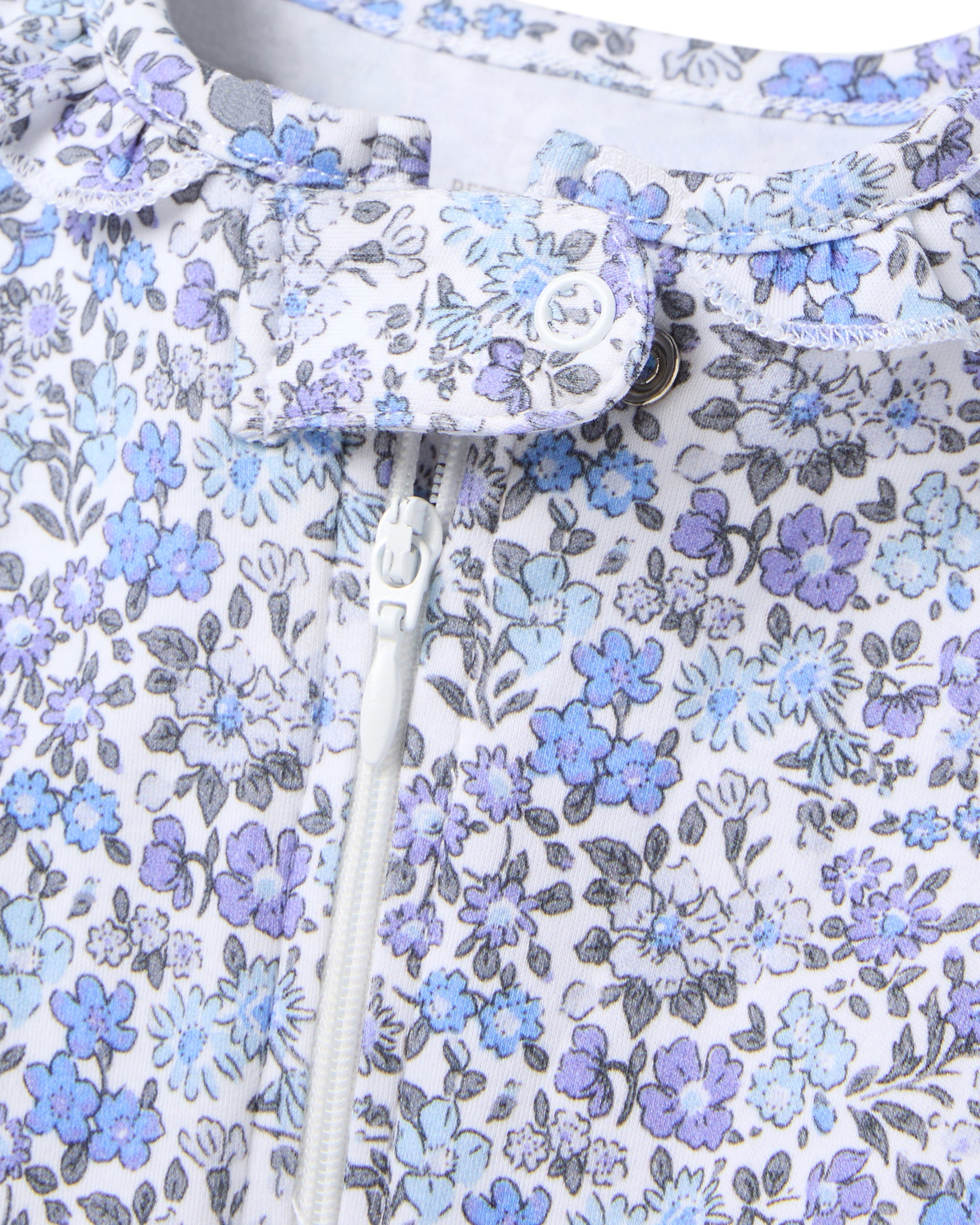 The Babys Pima Ruffle Collar Romper in Fleur dAzur by Petite Plume showcases a vintage-inspired floral print with vibrant blue and purple small flowers on a light background, featuring a vertical white zipper and a top buttoned flap.