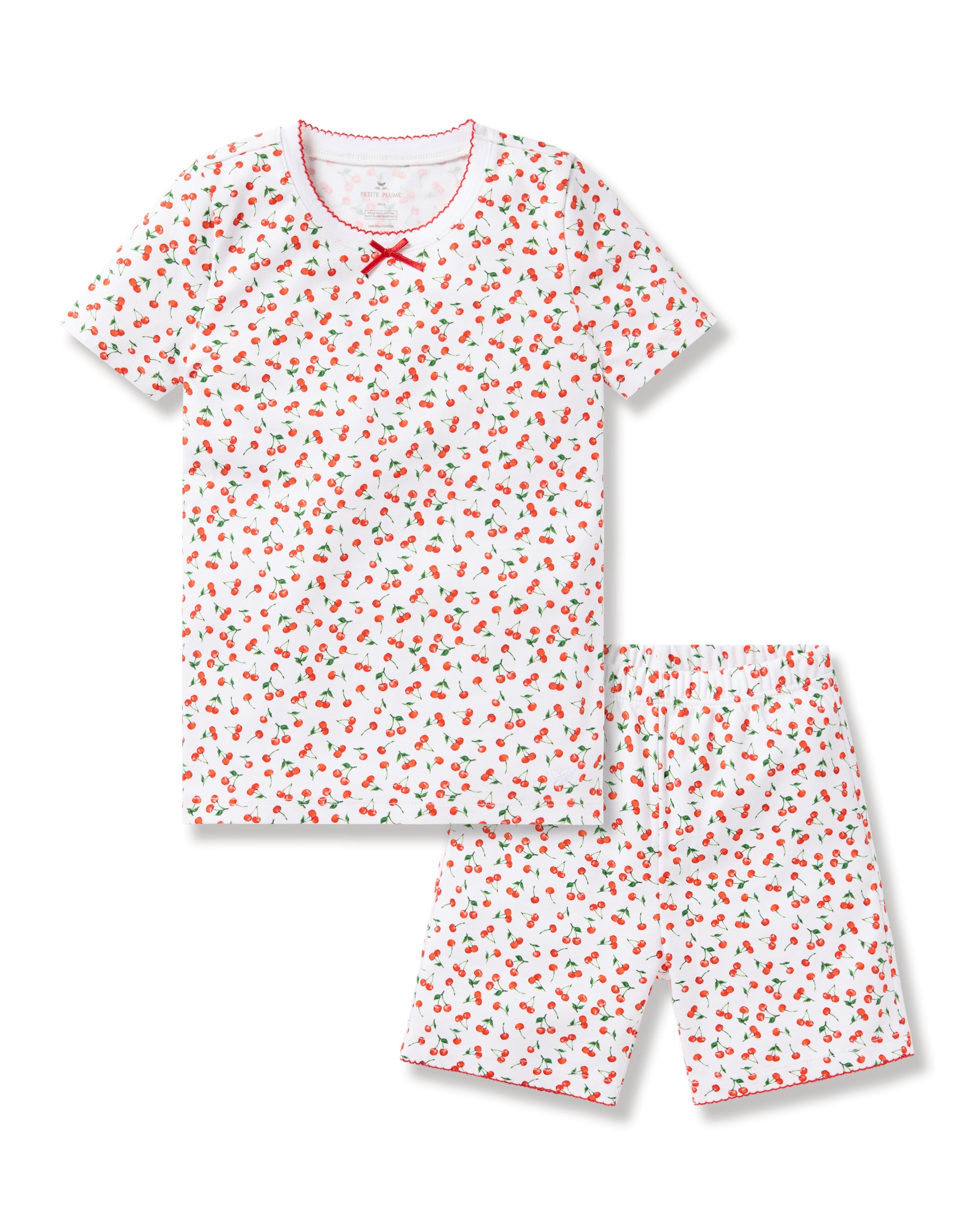 The Petite Plume Kids Pima Snug Fit Short Set in Cherry Orchard features a luxurious Pima Cotton design with a white base, playful red strawberry and green leaf pattern, stylish silhouette, red bow at the neckline, and matching red trim on the short-sleeved top and shorts.