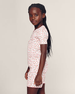 A young girl with long braided hair wears the Petite Plume Kids Pima Snug Fit Short Set in Cherry Orchard, standing in profile against a plain background, showcasing a stylish silhouette.