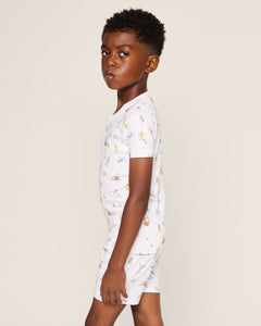 A young boy with short curly hair stands sideways in Petite Plumes Kids Pima Snug Fit Short Set in Easter Frolic, featuring soft Pima Cotton with small colorful prints. The plain off-white background highlights his profile and the luxurious fabric of the ensemble.