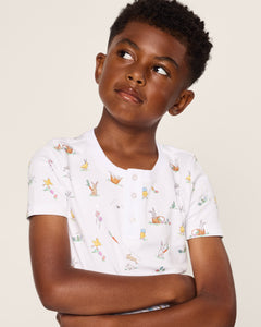 A young boy with short curly hair looks thoughtfully to the side, wearing a Petite Plume Kids Pima Snug Fit Short Set in Easter Frolic. His arms are crossed against a plain background, evoking playful simplicity.