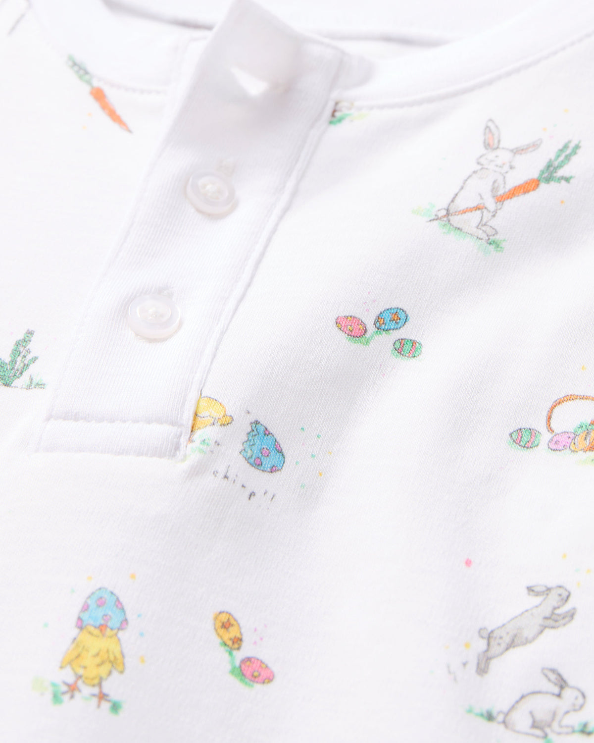 Close-up of Petite Plumes Kids Pima Snug Fit Short Set in Easter Frolic, crafted from soft Pima Cotton. This luxurious sleepwear displays Easter illustrations with a bunny holding a carrot, decorated eggs, and small chicks. Two charming buttons complete its playful design, ideal for children.