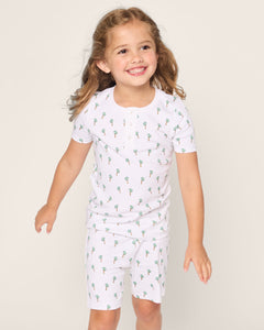 A young girl with long brown hair is wearing Petite Plumes Kids Pima Snug Fit Short Set in Palmier. She smiles, looking off to the side against a plain light background.