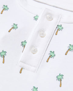 Close-up of the Kids Pima Snug Fit Short Set in Palmier by Petite Plume: white sleepwear shirt with a henley neck, four white buttons, soft Pima cotton, short sleeves, and small colorful palm trees scattered throughout.
