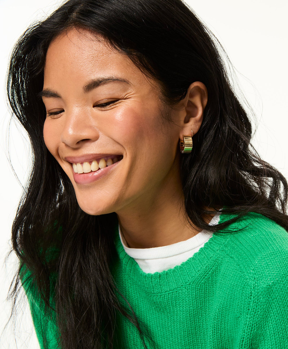 Close up side view of The Flat Cobra Huggie in Gold showcasing its flat profile on a smiling model against a white background