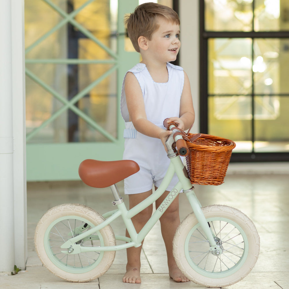Front view of James Henry Jon Jon on toddler in white piqué with Seaside Stripe trim, standing with mint balance bike